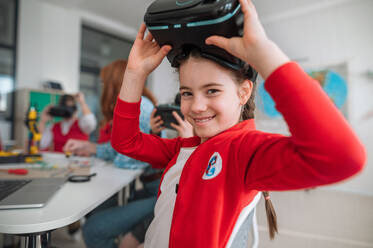 A happy schoolgirl wearing virtual reality goggles at school in computer science class - HPIF00040