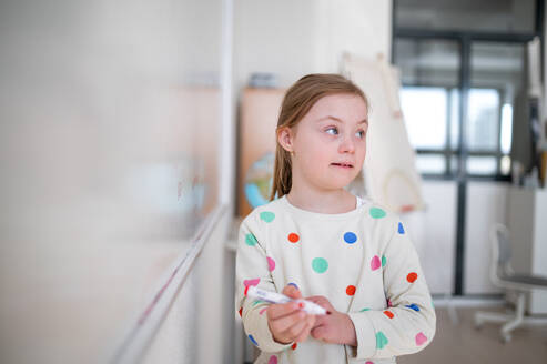 A little schoolgirl with down syndrome standing in front of whiteboard - HPIF00049