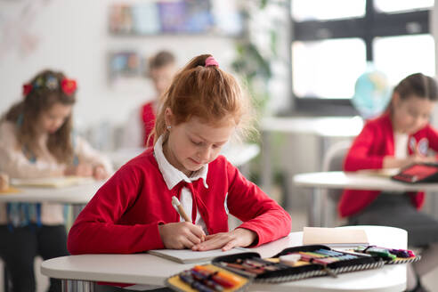 Eine Schülerin schreibt Notizen in ihr Notizbuch während des Unterrichts im Klassenzimmer in der Schule - HPIF00111