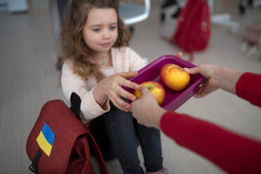 Ein kleines Mädchen bietet einer ukrainischen Klassenkameradin ihr Pausenbrot an, ein Konzept zur Aufnahme ukrainischer Kinder in Schulen. - HPIF00117