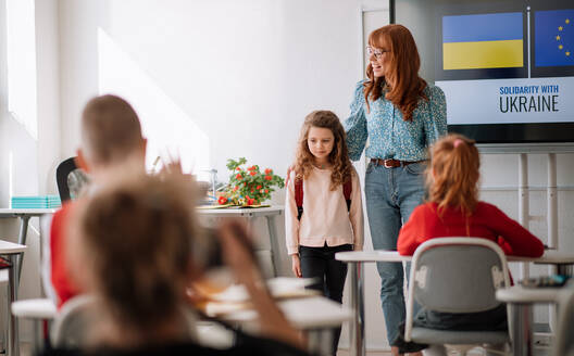 A teacher with Ukrainian schoolgirl in classroom, concept of enrolling and accpeting Ukrainian kids to schools. - HPIF00118