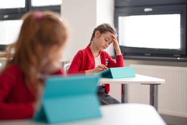 Ein gelangweiltes Schulmädchen benutzt ein digitales Tablet während einer Unterrichtsstunde in der Grundschule. - HPIF00124