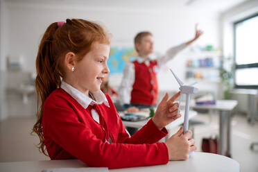 A schoolgirl holding wind turbine and learning about eco-friendly renewable sources of energy in classroom at school - HPIF00129