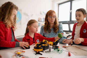 Eine Gruppe von Kindern mit einem jungen Lehrer für Naturwissenschaften programmiert elektrische Spielzeuge und Roboter im Robotik-Klassenzimmer - HPIF00131