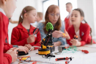 A group of kids with young science teacher programming electric toys and robots at robotics classroom - HPIF00132