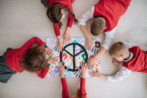 Draufsicht auf Kinder, die in der Schule ein Poster mit einem Friedenszeichen anfertigen. - HPIF00139