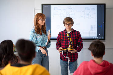 Ein College-Student präsentiert einem jungen Wissenschaftslehrer im Robotik-Klassenzimmer der Schule sein gebautes Roboterspielzeug. - HPIF00164
