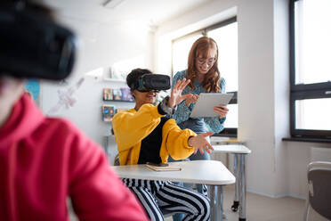 Junger Gymnasiallehrer unterrichtet Schüler mit VR-Brillen in einem Klassenzimmer - HPIF00173