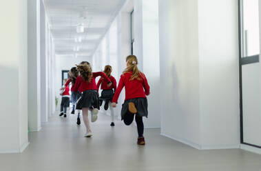 A rear view of schoolchildren in uniforms running in school corridor. - HPIF00184