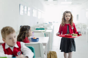 Ein glückliches Schulmädchen in Uniform hält ein Tablett mit Mittagessen in der Schulkantine. - HPIF00193