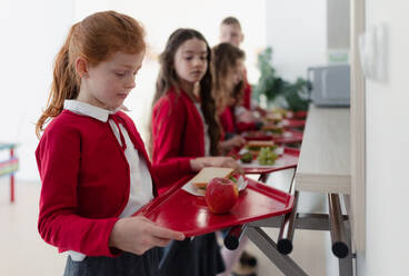 Glückliche Schulkinder stehen mit Tabletts in einer Schlange und erhalten ihr Mittagessen in der Schulkantine. - HPIF00196