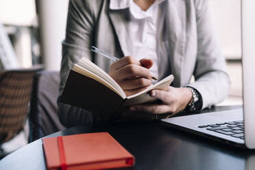 Young businesswoman writing in diary with pen at table in cafe - AMWF01043