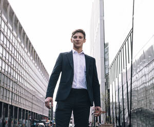 Confident businessman standing amidst buildings on road - AMWF01054