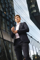 Contemplative young businessman standing in front of building - AMWF01059