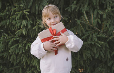 Besinnliches Mädchen mit Weihnachtsgeschenkkarton vor Tannenbaum - NDEF00219