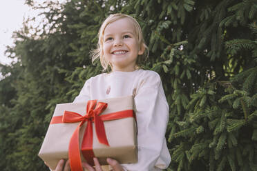 Glückliches Mädchen hält Geschenkbox in der Nähe von Tannenbaum - NDEF00220