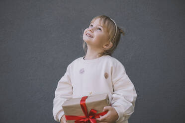 Lächelndes Mädchen schaut auf und hält eine Geschenkbox vor einer Wand - NDEF00225