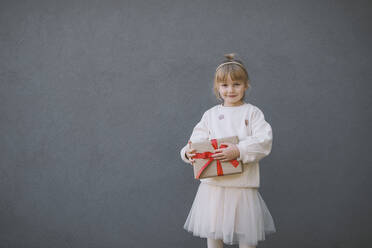 Mädchen mit Weihnachtsgeschenkbox vor einer grauen Wand - NDEF00226