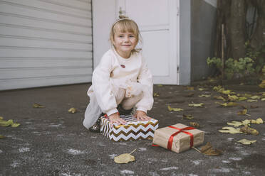 Lächelndes Mädchen mit Geschenkboxen auf der Straße hockend - NDEF00227