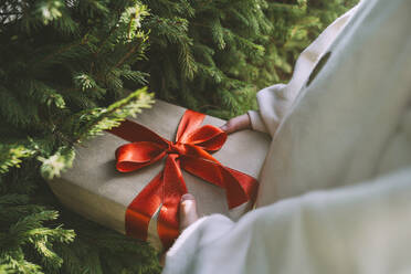 Mädchen hält Geschenk-Box mit Band in der Nähe von Tannenbaum gebunden - NDEF00236