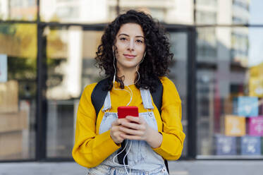 Junge Frau mit Handy in der Hand, die über In-Ear-Kopfhörer Musik hört - PGF01390