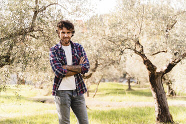 Smiling man with arms crossed in olive orchard - FMOF01548