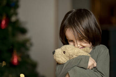 Glücklicher Junge umarmt Spielzeughund zu Hause - ANAF00583