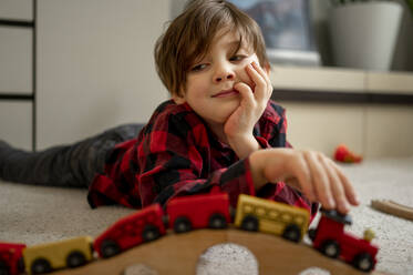 Süßer Junge spielt mit hölzernen Spielzeug Zug auf dem Boden zu Hause liegen - ANAF00587