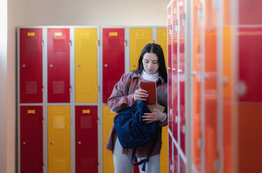 Ein Teenager-Student sitzt im Flur in der Nähe von bunten Schließfächer adn Verpackung Buch zu Rucksack in Campus Flur, zurück zu Schule Konzept. - HPIF00222