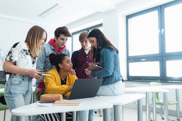 Gymnasiasten, die zusammen an einem Schreibtisch sitzen, einen Laptop benutzen und sich in der Pause im Klassenzimmer unterhalten. - HPIF00236