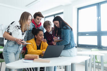 Gymnasiasten, die zusammen an einem Schreibtisch sitzen, einen Laptop benutzen und sich in der Pause im Klassenzimmer unterhalten. - HPIF00237