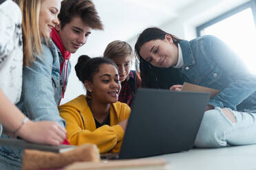 Gymnasiasten, die zusammen an einem Schreibtisch sitzen, einen Laptop benutzen und sich in der Pause im Klassenzimmer unterhalten. - HPIF00238