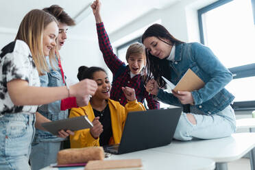 Gymnasiasten, die zusammen an einem Schreibtisch sitzen, einen Laptop benutzen und sich in der Pause im Klassenzimmer unterhalten. - HPIF00239