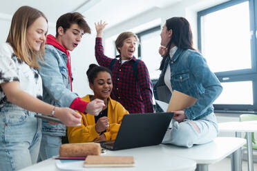 Gymnasiasten, die zusammen an einem Schreibtisch sitzen, einen Laptop benutzen und sich in der Pause im Klassenzimmer unterhalten. - HPIF00241