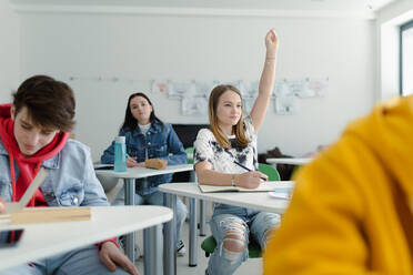 Aufmerksame Schülerinnen und Schüler, die in der Klasse sitzen und die Hände heben. - HPIF00249