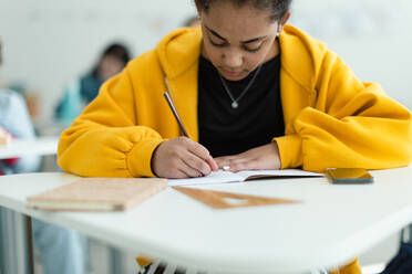 Aufmerksame Schüler in einer Klasse, die an ihren Tischen sitzen und Notizen schreiben, das Konzept 