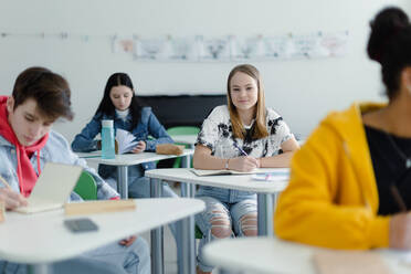 Aufmerksame Schüler in einer Klasse, die an ihren Tischen sitzen und Notizen schreiben, das Konzept 