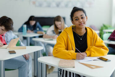 Aufmerksame Schüler in einer Klasse, die an ihren Tischen sitzen und Notizen schreiben, das Konzept 