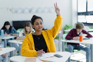 Aufmerksame Schülerinnen und Schüler, die in der Klasse sitzen und die Hände heben. - HPIF00254