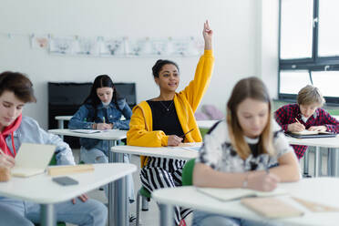 Aufmerksame Schülerinnen und Schüler, die in der Klasse sitzen und die Hände heben. - HPIF00255