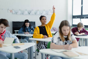 Aufmerksame Schülerinnen und Schüler, die in der Klasse sitzen und die Hände heben. - HPIF00255