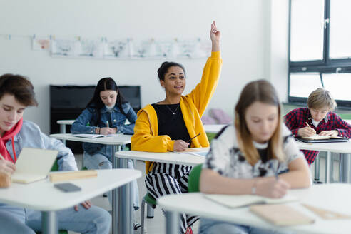 Aufmerksame Schülerinnen und Schüler, die in der Klasse sitzen und die Hände heben. - HPIF00255