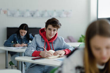 High school students paying attention in a class, sitting in their desks and writing notes, back to school concept. - HPIF00257