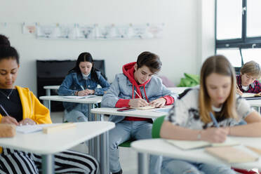 Aufmerksame Schüler in einer Klasse, die an ihren Tischen sitzen und Notizen schreiben, das Konzept 