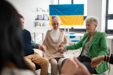 A group of seniors holding hands and praying for Ukraine together in church community center. - HPIF00347