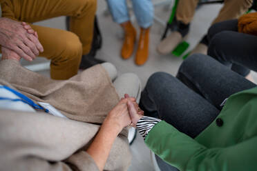 A group of seniors holding hands and praying for Ukraine together in church community center, close-up. - HPIF00357
