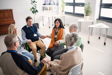 A group of senior people sitting in circle during therapy session, holding hands and praying together. - HPIF00360