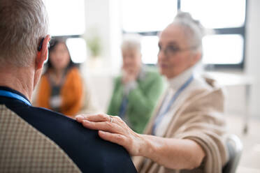 A group of senior people sitting in circle during therapy session, woman consoling depressed man. - HPIF00369