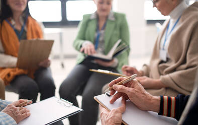 Excited elderly people attending a group therapy session at nursing house, positive senior man and woman sitting in circle, having conversation with psychologist - HPIF00372