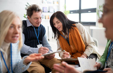 Excited elderly people attending a group therapy session at nursing house, positive senior man and woman sitting in circle, having conversation with psychologist - HPIF00375